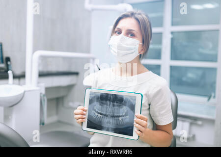 Portrait of female dentist .She standing in her dentist office and showing an x-ray of the jaw and teeth on the tablet pc Stock Photo