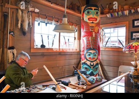Norwegian-Tinglit carver Jeff Skaflestad at a work table within the Icy Strait Point Cannery Museum. The totem in the corner is entitled 'Hawkt' Tooth Warrior'. Icy Strait Point, Alaska, USA Stock Photo