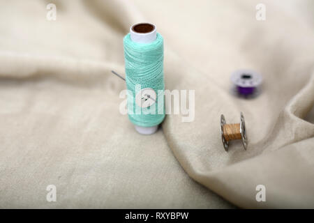 Portrait of sewing thread, button and two bobbins on the cloth. Stock Photo