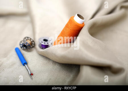 Photo of one orange thread, needle ripper and bobbin on the cloth. Stock Photo