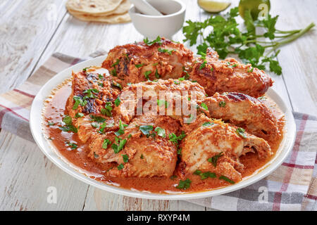 Kuku Paka, Kenyan chargrilled Chicken in creamy spicy Coconut gravy served on a white plate on an old wooden table, view from above, close-up Stock Photo