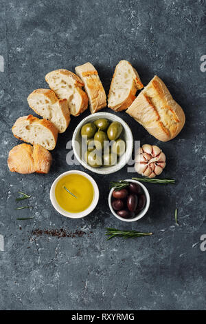 Italian food concept. Cooking Italian bruschetta. Olives, fresh baguette slices, olive oil, garlic and rosemary on dark stone background top view Stock Photo