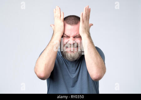 Mature bearded man standing and clenching head from a migraine attack Stock Photo