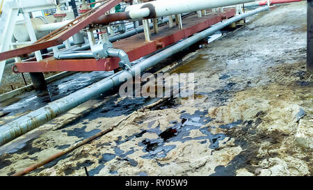 Spilled oil on sandy soil near pipelines and process equipment. Oil leaks during operation and repair Stock Photo