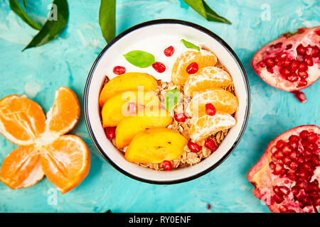 Tropical  smoothies bowl  fruit Breakfast homemade granola yogurt pomegranate, tangerine, persimmon on blue background. healthy organic layered desser Stock Photo