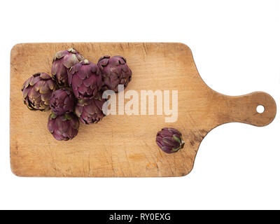Raw artichokes, Mediterranean vegetable, uncooked on wooden cutting board. Isolated on white. Stock Photo