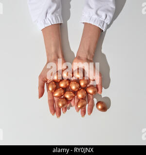 The hands of the girl hold golden painted eggs as a symbol of wealth and profit. Around the gray background with space for text. Stock Photo
