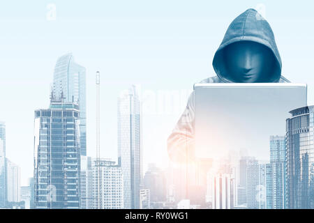 Double exposure of hacker in black hoodie holding laptop and modern city with skyscrapers background Stock Photo