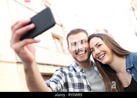 Happy couple taking selfies with smart phone standing in the street Stock Photo