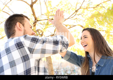 Happy friends or couple giving high five outdoors in a park Stock Photo
