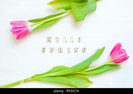 Spring flower background - composition made of yellow tulip flowers and wooden inscription Hello Spring on the white background. Flat lay, top view Stock Photo