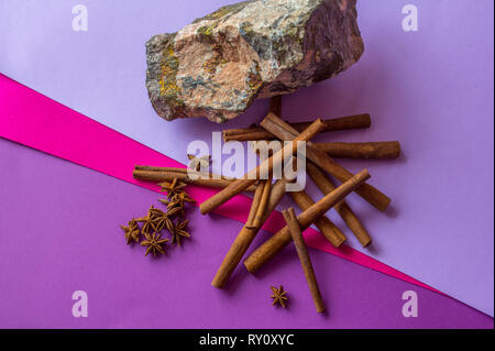 Still life of stone, cinnamon sticks and anise stars lying on coloured background Stock Photo