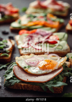 Close up view of different sandwiches with meat, egg, vegetables and herbs. Copy space for text. Assortment meat toasts on black background. Idea, creative concept for sausage maker. Vertical Stock Photo