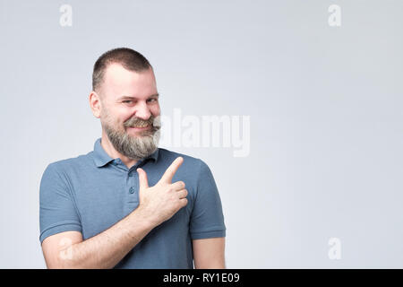 MAture strong man with beard in blue shirt pointing a side with surprised face expression Stock Photo