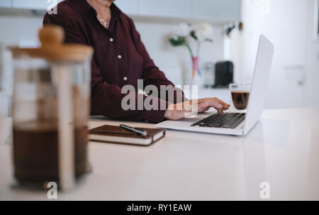 Close up mature woman hands typing on her laptop, in the kitchen Stock Photo