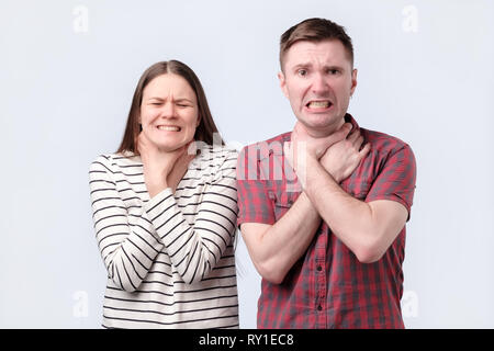 throat pain. Two sick young woman and man standing holding neck because feeling pain. Stock Photo