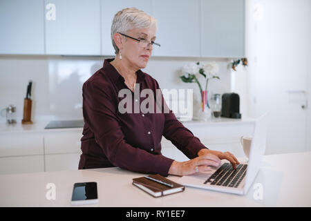 Beautiful senior woman using laptop computer at home, browsing internet. Elderly lady typing on computer keyboard and surfing the net Stock Photo