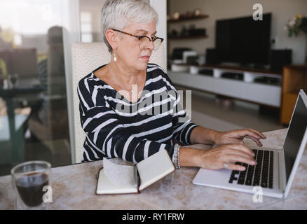 Beautiful senior woman using laptop computer at home, browsing internet. Elderly lady typing on computer keyboard and surfing the net Stock Photo