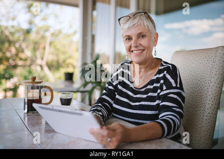 Portrait of a mature woman smiling, using her tablet at home , outside on the balcony. Beautiful elderly woman smiling looking into the camera Stock Photo