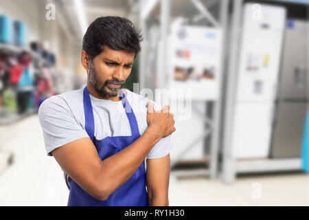 Indian man working at supermarket or hypermarket holding painful shoulder with hand and hurting expression Stock Photo