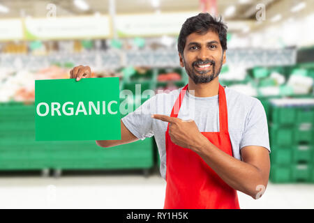 Indian man working at grocery store or supermarket presenting organic text on green paper as advertising products concept Stock Photo