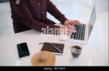 Close up of mature woman hands typing on her laptop, in the kitchen. With notebook, smartphone and coffee Stock Photo