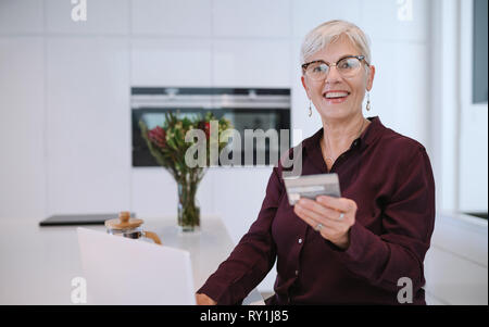 Happy senior woman making online payments of bill using laptop. Smiling mature woman shopping online with credit card. Pensioner holding credit card f Stock Photo