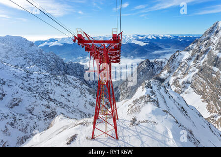 Red Cable Car Pylon and cables way at mountains landscape. Blue sky and massive mountains in background during winter day in ski resort Stock Photo