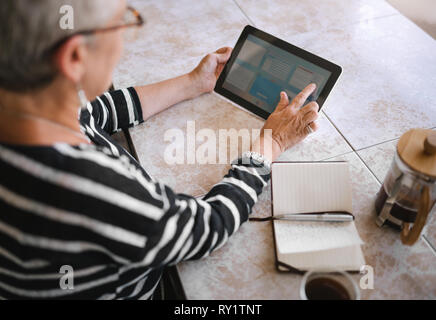 Top view of mature woman making notes interacting on a digital tablet Stock Photo