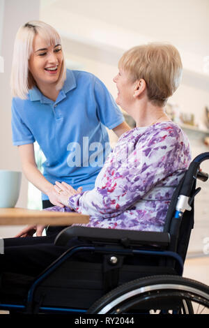 Female Care Assistant Talking To Senior Woman Sitting In Wheelchair At Home Stock Photo