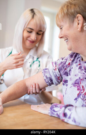 Female Nurse Giving Senior Woman Injection In Arm With Syringe Stock Photo