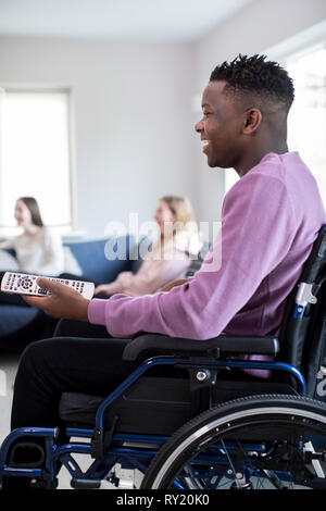 Teenage Boy In Wheelchair Watching Television With Freinds At Home Stock Photo