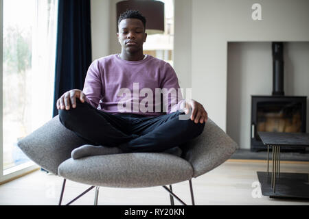 Close Up Of Peaceful Teenage Boy Meditating Sitting In Chair At Home Stock Photo