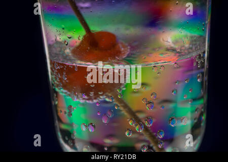 Interesting stress patterns in plastic wine glass seen with red cherry on cocktail stick in gin and tonic drink giving weird appearance Stock Photo