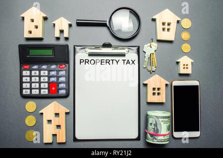 Table with wooden houses, calculator, coins, magnifying glass with the word Property Tax. Property taxes. Calculation of interest on housing tax. Pena Stock Photo