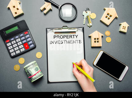 Table with wooden houses, calculator, coins, magnifying glass with the word Property investments. Attracting investment in your home. Repair planning. Stock Photo