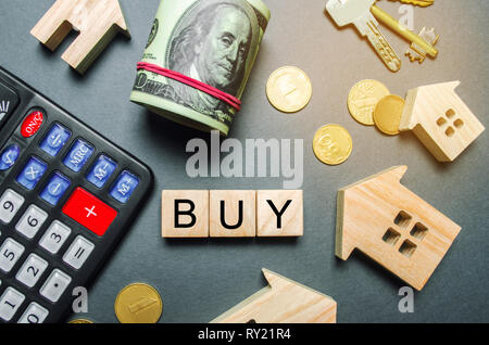 Wooden houses, a calculator, keys, coins and blocks with the word Buy. Buying a house or apartment. Buy property/ affordable housing. Realtor Services Stock Photo