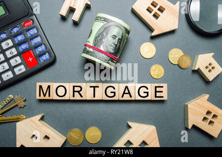 Wooden houses, a calculator, keys, coins and blocks with the word Mortgage. Buying a home in debt. Purchase a house on credit. Loan on the property. I Stock Photo