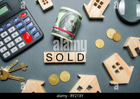 Wooden houses, a calculator, keys, coins and blocks with the word Sold. Concept of selling a house, apartment. Market of real estate. Trade of propert Stock Photo