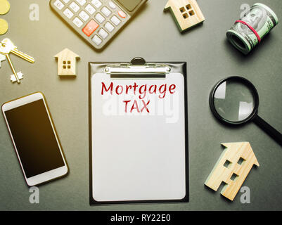 Table with wooden houses, calculator, coins, magnifying glass with the word Mortgage Tax. Property taxes. Calculation of interest on housing tax. Pena Stock Photo