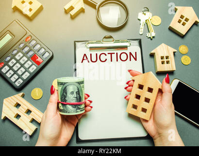 Table with the word Auction. The women auctioneer is holding money in the hands of dollars and a wooden house. Purchase and public sale of real estate