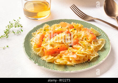 Pasta and wine, Italian dinner. Farfalle with smoked salmon and cream sauce, with a glass of wine Stock Photo