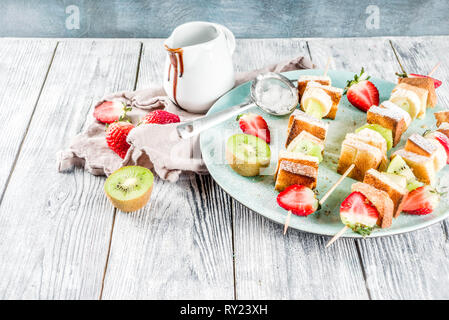 Summer breakfast snack. Fruit vegan dessert kebabs on skewers with toast French fried bread, fruits and berries. With powdered sugar and chocolate sau Stock Photo