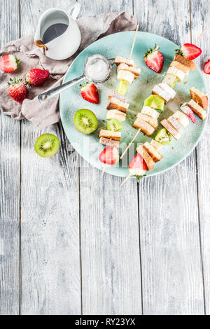 Summer breakfast snack. Fruit vegan dessert kebabs on skewers with toast French fried bread, fruits and berries. With powdered sugar and chocolate sau Stock Photo