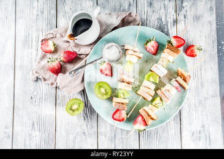 Summer breakfast snack. Fruit vegan dessert kebabs on skewers with toast French fried bread, fruits and berries. With powdered sugar and chocolate sau Stock Photo