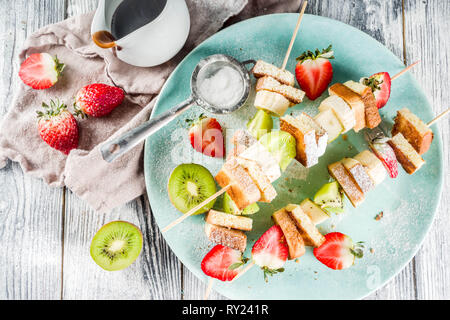 Summer breakfast snack. Fruit vegan dessert kebabs on skewers with toast French fried bread, fruits and berries. With powdered sugar and chocolate sau Stock Photo