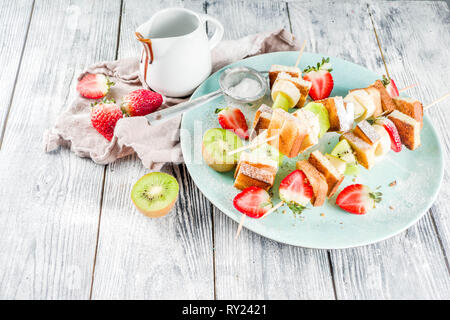 Summer breakfast snack. Fruit vegan dessert kebabs on skewers with toast French fried bread, fruits and berries. With powdered sugar and chocolate sau Stock Photo