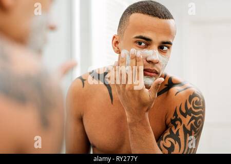 Young man applying anti-aging cream on his face Stock Photo