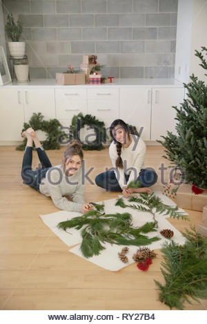 Portrait happy teenage girls making christmas swags on floor