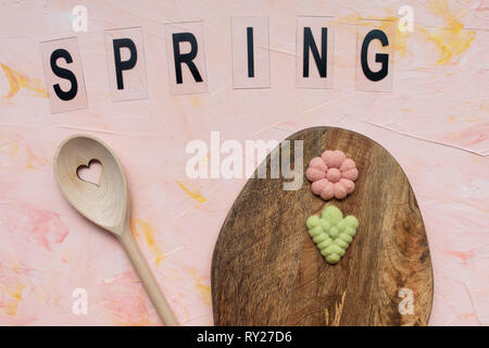 SPRING word, stirring spoon and flower cookies on a wooden board on a pink background . Spring holidays cooking concept. Top view, flat lay. Stock Photo